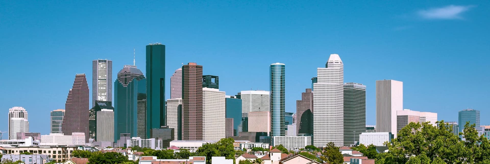 Downtown Houston skyline with modern skyscrapers under a clear blue sky and trees below.